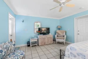 Wavecrest Bedroom blue and white suite with a big tv, wicker rocking chair, and ceiling fan - Windemere Inn Florida bed and breakfast