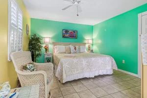 Windsong Bedroom green and yellow suite with a queen bed, wicker chair, and a ceiling fan - Windemere Inn Florida bed and breakfast