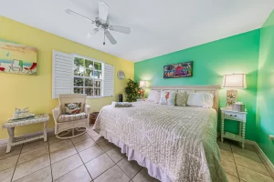 Windsong Bedroom green and yellow suite with a ceiling fan, a queen bed, and wicker chair - Windemere Inn Florida bed and breakfast