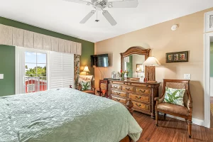 Melbourne Bedroom green and tan suite with a ceiling fan, a large dresser, and chairs - Windemere Inn Florida bed and breakfast