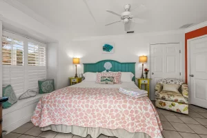 North Beach Bedroom orange and white suite with a king bed, cloth chair, ceiling fan, and window - Windemere Inn Florida bed and breakfast