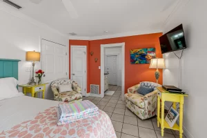 North Beach Bedroom orange and white suite with a sitting area, mounted tv, and a king bed - Windemere Inn Florida bed and breakfast