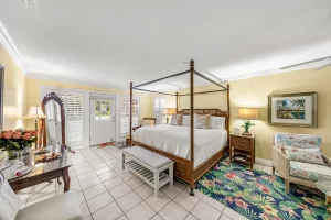 Seabreeze Bedroom yellow and white suite king sized bed, bench, table, standing mirror , and sitting area with glass table and wicker chair - Windemere Inn Florida bed and breakfast