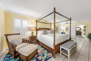 Seabreeze Bedroom yellow and white suite king sized bed, bench, and chair with foot rest - Windemere Inn Florida bed and breakfast