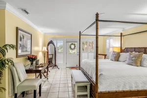 Seabreeze Bedroom yellow and white suite king sized bed, bench, door to the porch, table and standing mirror - Windemere Inn Florida bed and breakfast