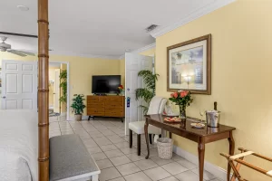 Seabreeze Bedroom yellow and white suite front table, bed and bench, ceiling fan, and dresser with tv - Windemere Inn Florida bed and breakfast